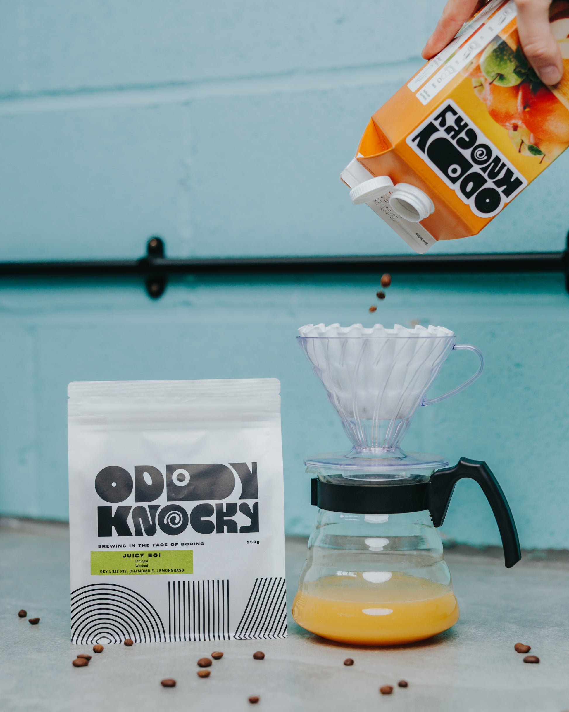 Ethiopian washed coffee Juicy Boi being brewed with fresh orange juice and coffee beans scattered around.