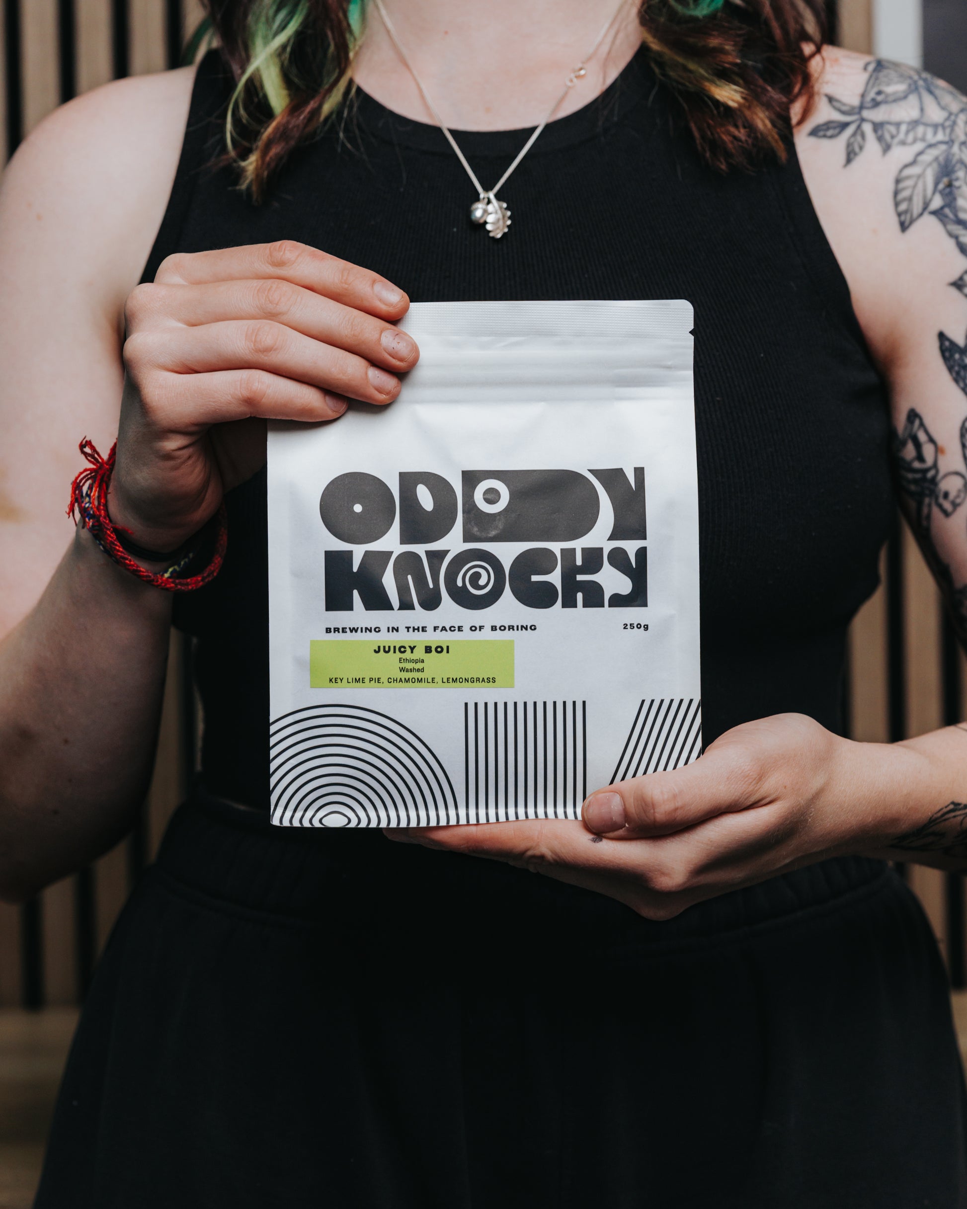Ethiopian washed coffee Juicy Boi bag held by a person with tattoos in a stylish black outfit.