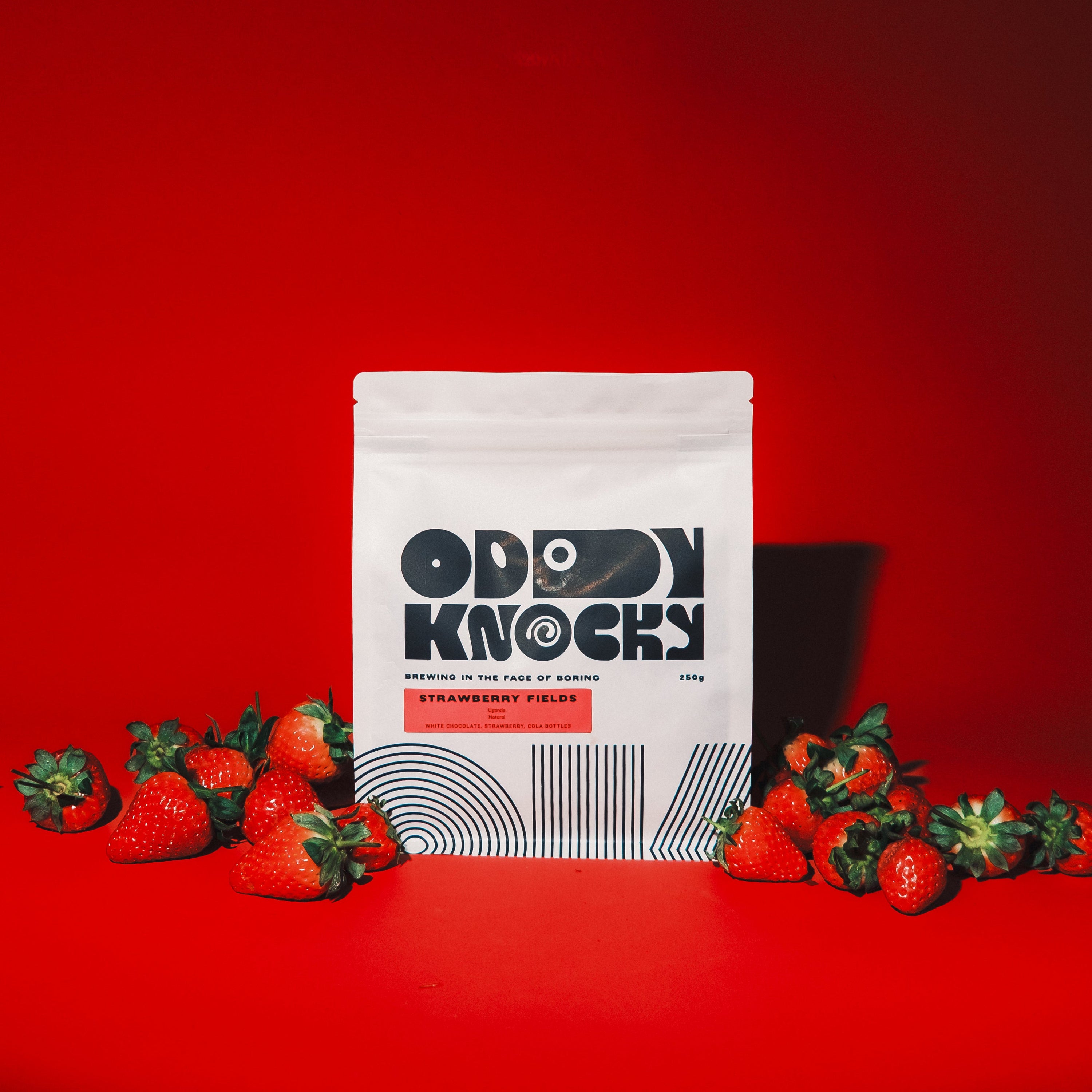 Strawberry Fields coffee packaging with fresh strawberries on a bold red background.