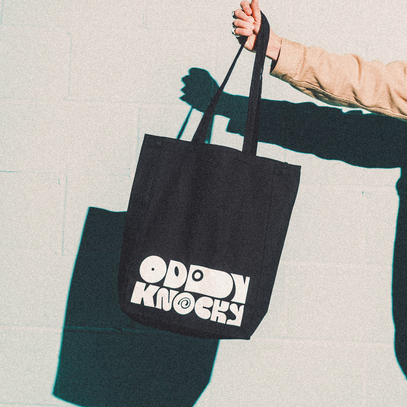 Tote Bag featuring Oddy Knocky design, being held against a textured background.